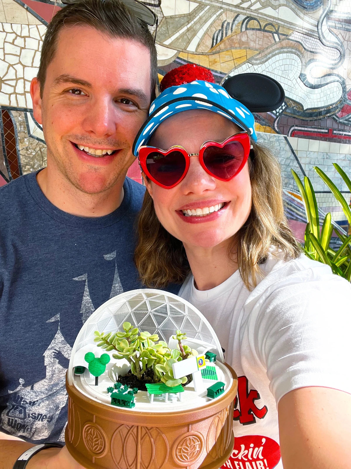 Chris and Laura holding their Land Planter in front of a mosaic mural